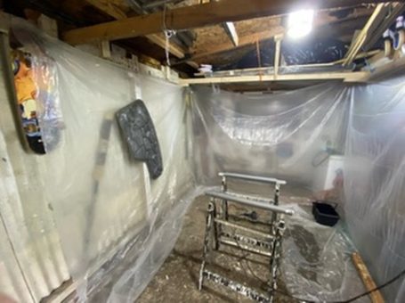A cluttered workspace covered in plastic sheeting, with tools and a ladder visible.
