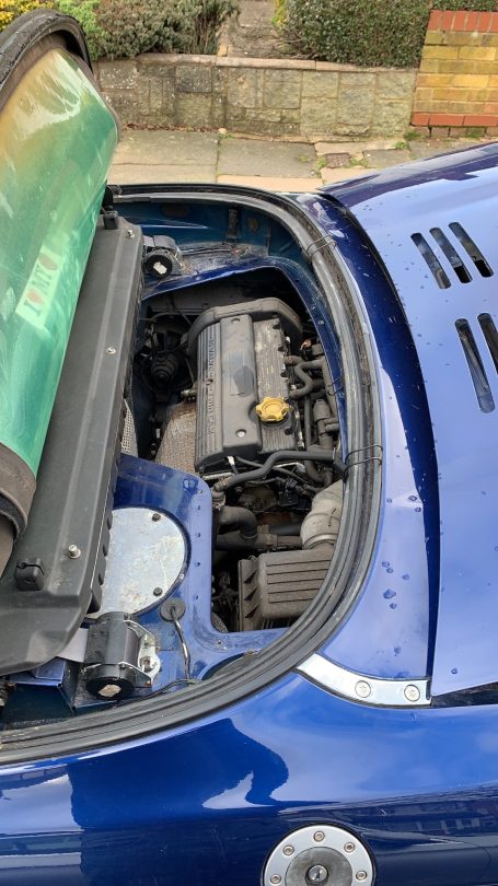 View of a car engine compartment, featuring a dark engine and a partially open hood.
