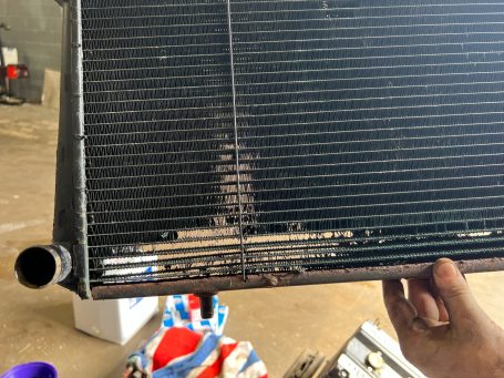 Hand holding a metal radiator with visible damage and a cooling pipe.