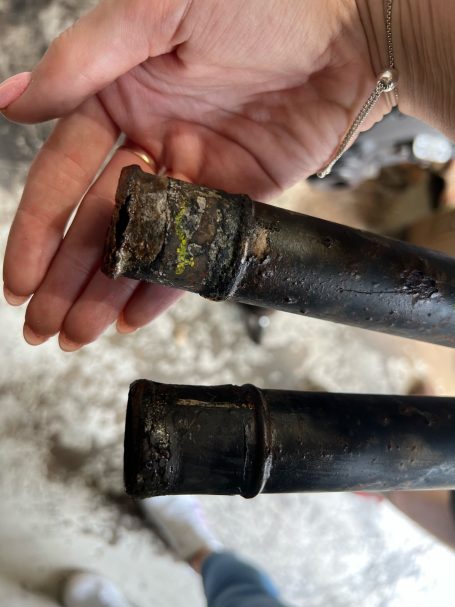 Close-up of a hand holding two metal pipes, one with a yellow mark.