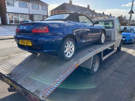 A blue convertible car loaded onto a tow truck on a residential street.