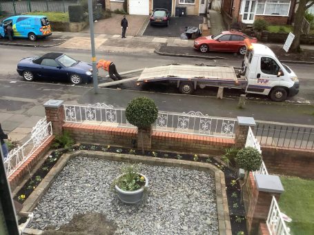 White recovery truck loading a blue car on a residential street.