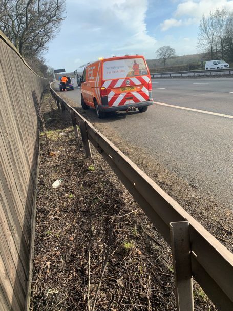 Orange van parked beside a road with a guardrail and trees in the background.