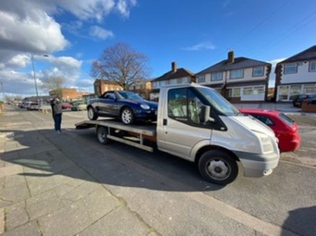 A tow truck with a blue car on its flatbed parked on a residential street.