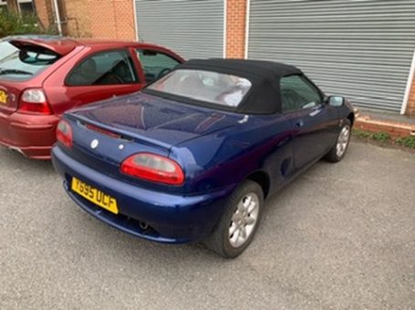 Blue convertible car parked beside a red hatchback in a driveway.