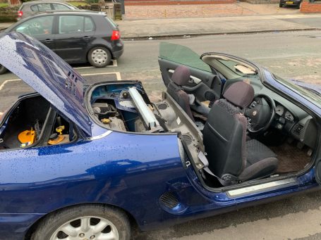 Blue convertible car parked on the street, with the roof and trunk open.