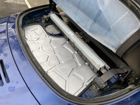 View of a car trunk with a battery pack installed, showing metal casing and connections.