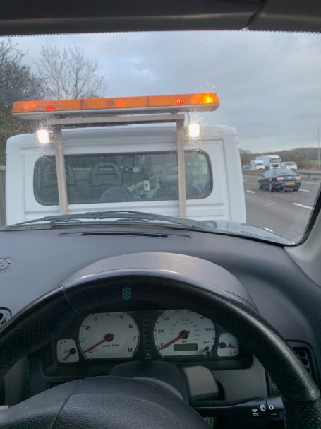View from inside a vehicle, showing a tow truck ahead with warning lights activated.