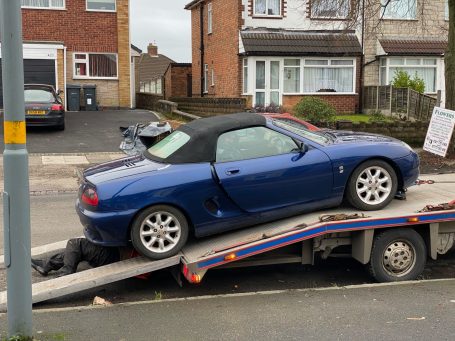 Blue convertible sports car being loaded onto a tow truck.
