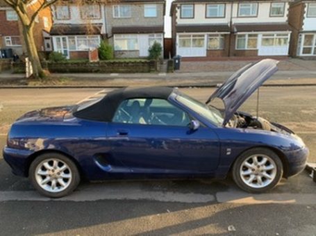 Blue convertible car parked on the street with the bonnet open.