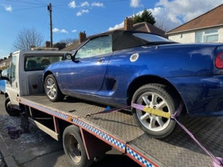 A blue convertible car being transported on a tow truck.