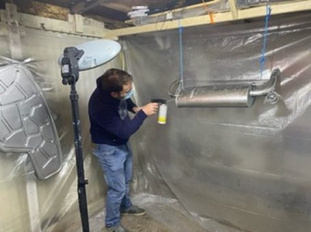A person spraying a metallic object in a well-prepared workshop space.
