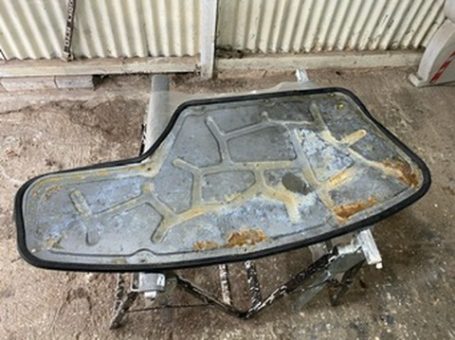 Rusty metal tray with an irregular shape and a worn surface, resting on a workbench.