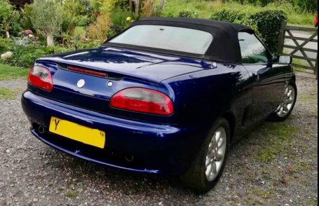 Blue convertible sports car parked on a gravel driveway.