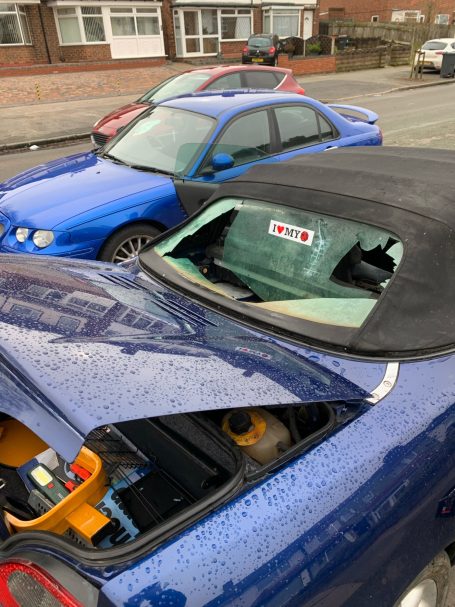 A blue convertible car with a damaged rear window parked near another blue car.