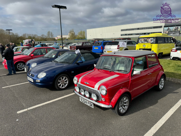 A red Mini, a blue sports car, and other classic cars parked in an event area.